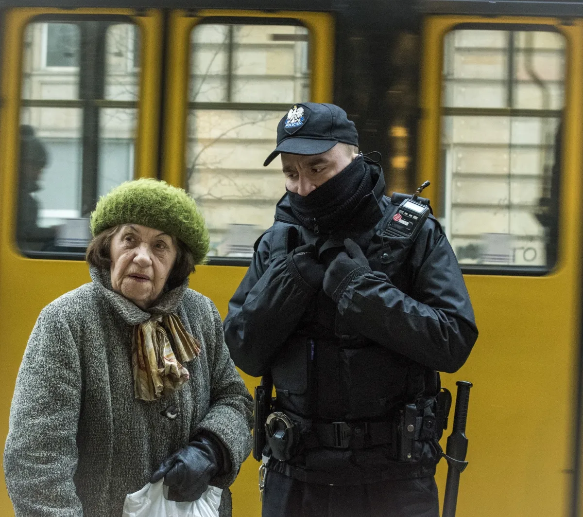 Elderly woman beside an armed police officer and a yellow tram